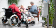 Ein Desinfektionsspender, im Hintergrund alte Menschen im Rollstuhl.