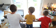 e Mutter des sechsjährigen Jakob und des vierjährigen Valentin arbeitet Zuhause an einem Laptop, während ihre Kinder neben ihr malen und ein Buch ansehen.