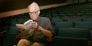 Ein Mann sitzt in einem Theaterraum, ein Buch in der Hand.