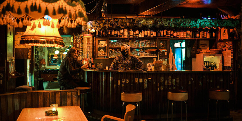 Blick auf den Tresen in Rosis Bar. Eine Frau sitzt am Tresen, eine Frau mit Mundschutz steht hinterm Tresen