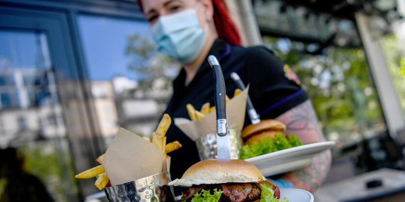 Kellnerin mit Mundschutz bringt Burger