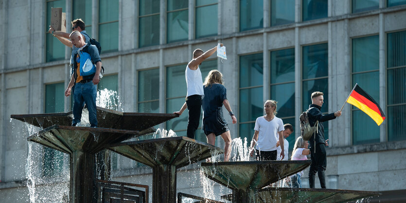 Demonstrant:innen sind auf einen Brunnen gekletter: Den Brunnen der Völkerverständigung am Alexanderplatz, einer trägt eine Deutschlandflagge.