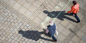 Ein Mann und eine Frau laufen über das auf das Pflaster gemalte Wort "Abstand"