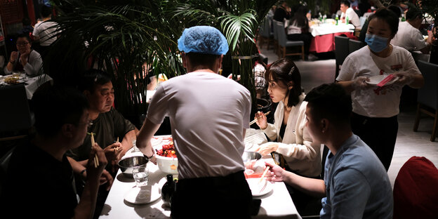 Vier Menschen an einem Tisch im Restaurant, die von einem Kellner bedient werden