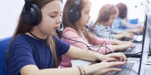Mädchen sitzen mit Headset und Kopfhörern nebeneinander vor Computern