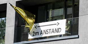 Auf einem Balkon hängt ein Schild mit der Aufschrift "2m Anstand".