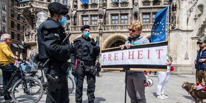 Corona-Demonstranten in München: Ein Mann steht vor zwei Polizisten und hält ein Schild mit dem Wort Freiheit hoch