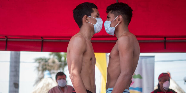Zwei Boxer mit Maske stehen sich vor dem Wiegen gegenüber