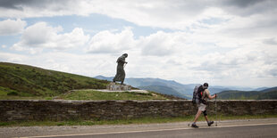 Ein Wanderer vor einer Statue eines Pilgers.