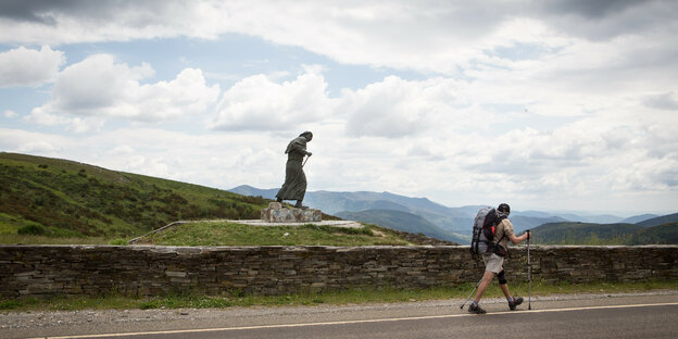 Ein Wanderer vor einer Statue eines Pilgers.