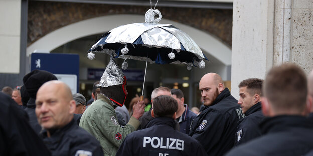 Polizisten stehen um einen Menschen mit einem Regenschirm