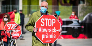 Ein älterer Demonstrant demonstriert mit Maske und einem Schild gegen die Abwrackprämie