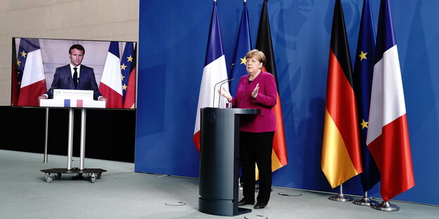 Merkel spricht an einem Pult, Macron ist auf einem Bildschirm zu sehen