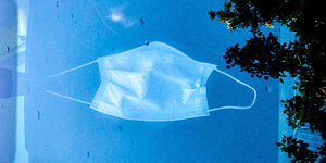 Eine Nase-Mund-Schutzmaske in Großaufnahme vor blauem Himmel – sie scheint zu fliegen