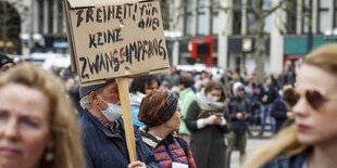 Mehrere Personen auf einer Demo und ein Schild, das vor Zwangsimpfungen warnt