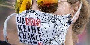 Eine Frau trägt Sonnenbrille und Maske mit der Aufschrift "Gib Gates keine Chance"