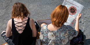 zwei frauen sitzen auf dem boden, eine ließt eine Zeitung