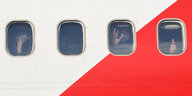 Menschen mit Schutzmaske hinter den Fenstern eines Flugzeugs.