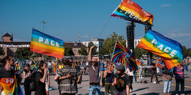 Demonstrantinnen und Demonstranten schwenken in Stuttgart Regenbohnenfahnen