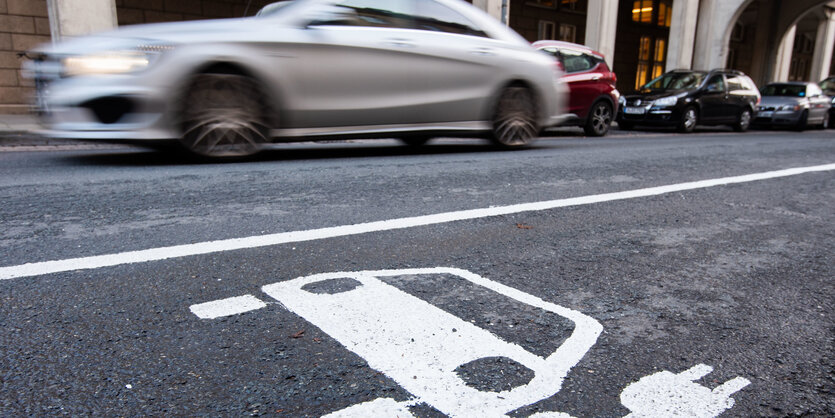 Ein Symbol eines Elektroautos markiert einen Parkplatz neben einer E-Ladesäule.