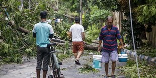 Ein Mann trägt frisches Trinkwasser eine Straße entlang, die zuvor durch die heftigen Winde des Zyklons verwüstet worden ist.