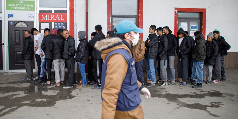 Ein Mann mit Mundschutz passiert eine Menschenschlange.