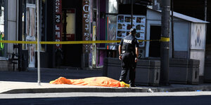 Ein Polizist steht neben einem toten Menschen, der mit einem orange-farbenen Tuch bedeckt ist