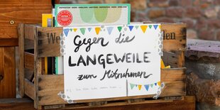 Das Bild zeigt eine Bücherkiste aus Holz mit der Aufschrift: Gegen die Langeweile zum Mitnehmen