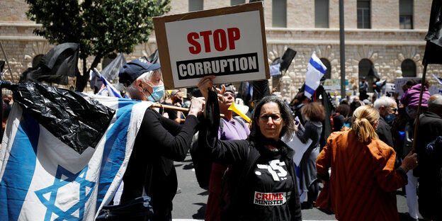 Auf einer Demo hält eine Frau hält ein Plakat hoch, auf dem steht "Stop Corruption"