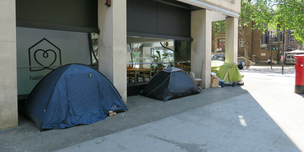 Drei Zelte stehen vor einen geschlossenen Geschäft in London.