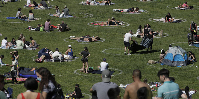 Menschen sitzen mit striktem Sicherheitsabstand im Park