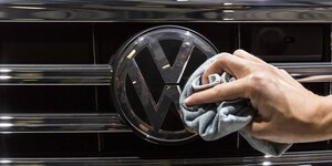 Eine Hand putzt das VW-Logo an der Kühlerhaube eines Autos