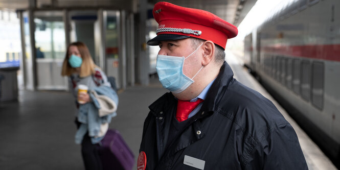 Schaffner mit Mundschutz am Bahnsteig