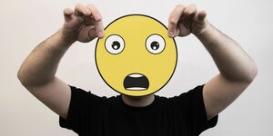 Jemand hält sich ein "Schock-Emoji" vors Gesicht