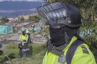 Polizisten in Warnwesten und mit Helmen stehen am Rande einer Favela.