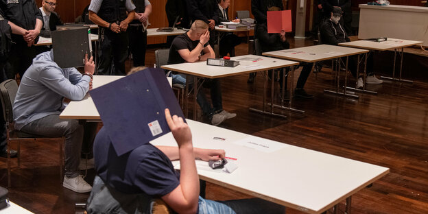 Justizwachtmeister stehen im Kornhaus hinter jungen Männern, die sich Aktenordner vor das Gesciht halten Justizwachtmeister stehen im Kornhaus hinter jungen Männern, die sich Aktenordner vor das Gesciht halten
