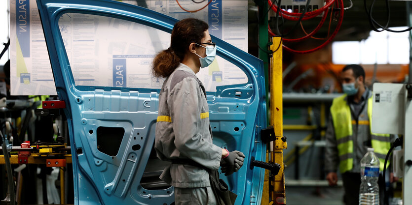 Ein Arbeiter in einem Automobilwerk geht an einer Autotür vrobei