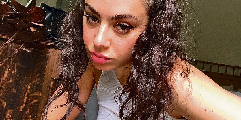 Charli XCX trägt pinkfarbenen Lippenstift und ein Männerunterhemd.