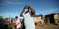 Ein Mann zieht sich eine Mundschutzmaske an, er steh auf einer Strasseneben ärmlichen Hütten