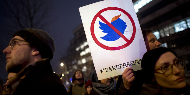 Demonstranten halten ein Plakat mit einem verfremdeten Twitter-Symbol