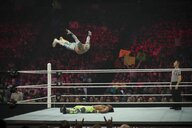 Zwei Wrestler im Ring. Einer macht einen Diving Headbutt, er springt von oben mit ausgebreiteten Armen auf seinen am Rücken liegenden Gegner