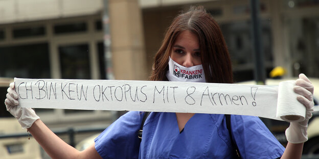 Eine Frau mit Mundschutz und im Pflegekittel hält ein Spruchband auf dem steht: "Ich bin kein Oktopus mit acht Armen."