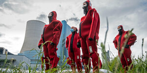 Männer in roten Neoprenanzügen stehen vor einem Kohlekraftwerk