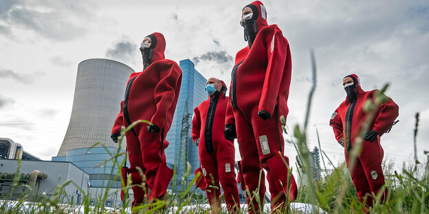 Männer in roten Neoprenanzügen stehen vor einem Kohlekraftwerk