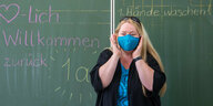 Eine Lehrerin mit Mundschutz vor einer Tafel.