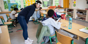 Lehrrerin mit Gesichtsschutz aus Plastik beugt sich zu einem Schüler