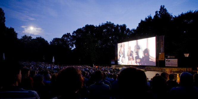 menschen sitzen in einem Openairkino vor einer Leinwand