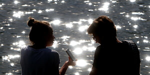Zwei Menschen mit Smartphone am Wasser.