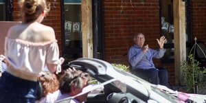 Drive-Thru in Großbritannien: Eine junge Frau winkt aus einem fahrenden Auto einem sitzenden alten Mann vor dem Pflegeheim zu