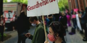 Eine Frau hält bei einer Kundgebung ein Schild, auf dem Gesundheitskrise steht